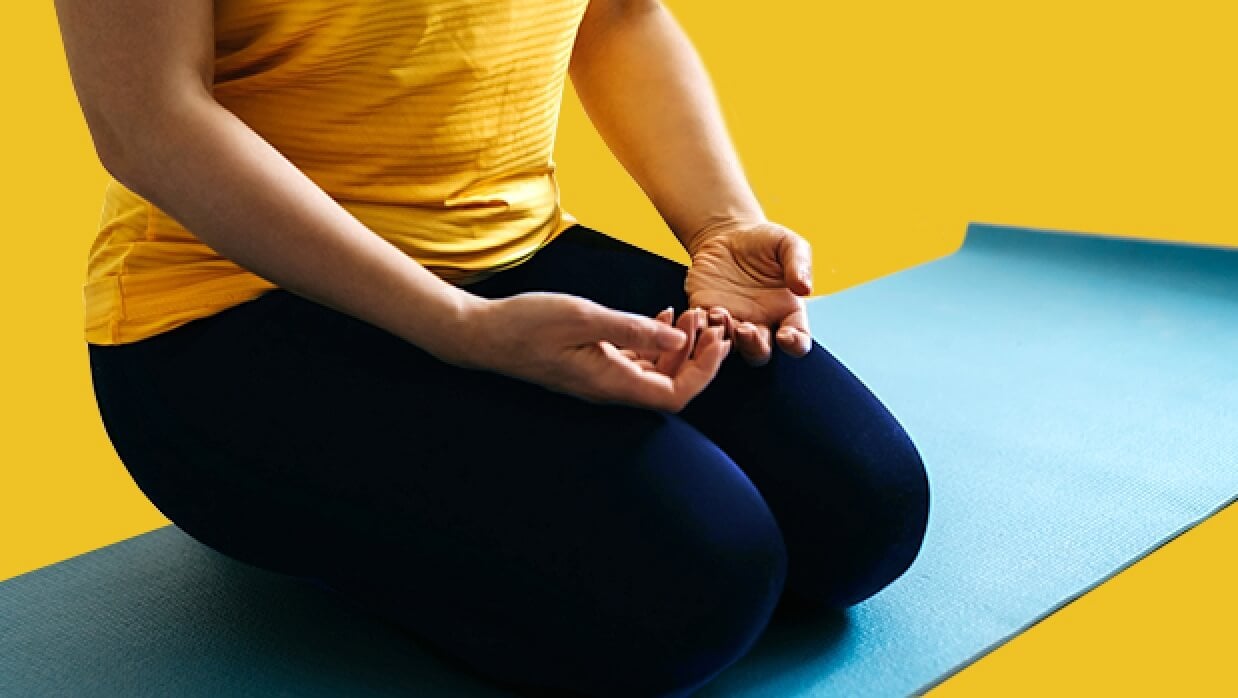 Person kneeling with hands palm-up in their lap on a yoga mat